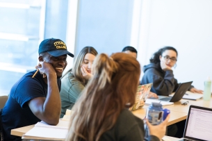 Ithaca College students sit at long tables together in a classroom.